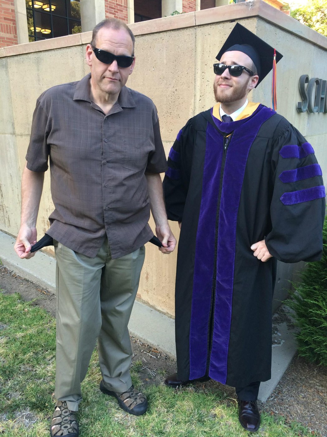 Trevor in his graduation cap and gown, standing beside his dad, Tom